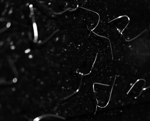 Black and white close-up of thin, bent wire fragments scattered across a dark, sparkling surface.