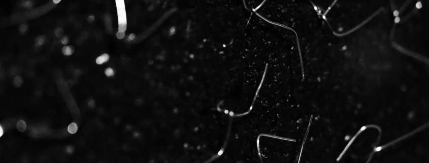 Black and white close-up of thin, bent wire fragments scattered across a dark, sparkling surface.